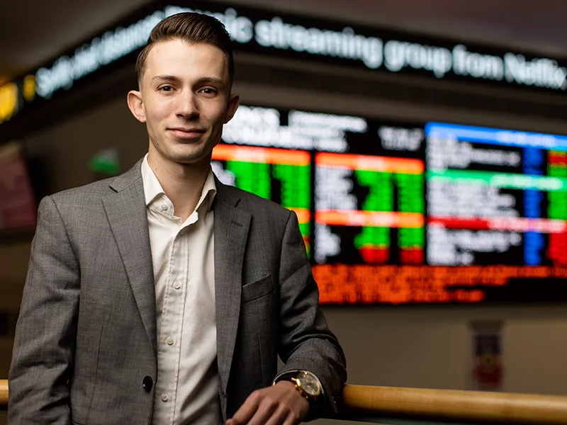 student in suit posing in front of digital stock ticker