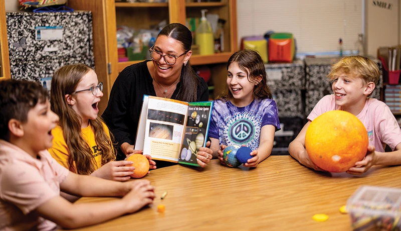 teacher showing 4 young students a science book