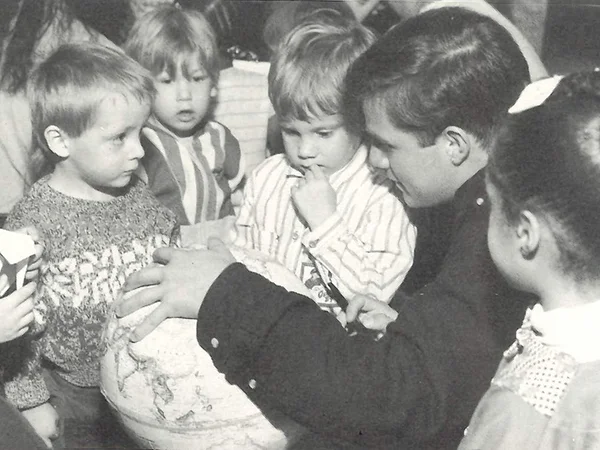 archival photo of college student holding globe surrounded by children