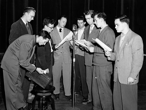 archival photo of students around a radio microphone in the 1950s