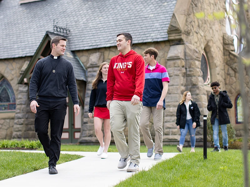 students walking with a Catholic priest on campus