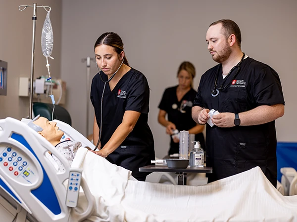 Nursing program students posing with a dummy on a hospital bed