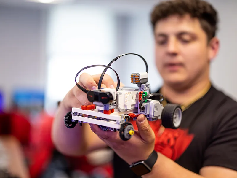 student displaying a Lego vehicle equipped with robotics