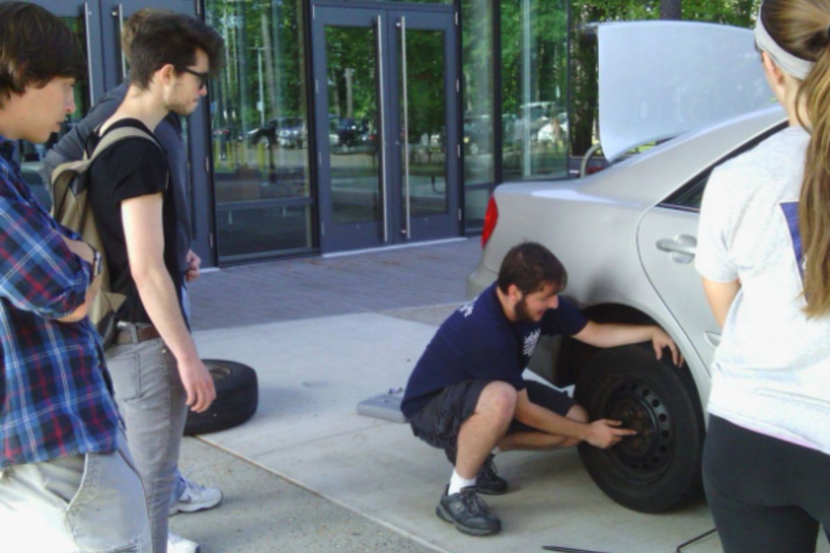 Students learning how to change a car tire. 